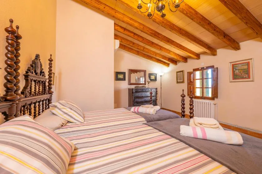 Un dormitorio con ropa de cama a rayas, vigas de madera vistas y una ventana.