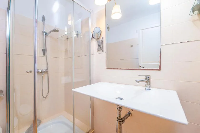 Un baño luminoso con ducha de vidrio y un lavabo blanco bajo un espejo.