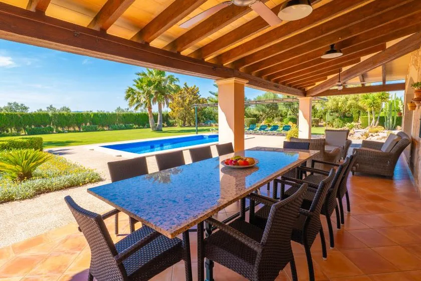 Una zona de comedor exterior cubierta da a una piscina y un jardín ajardinado.