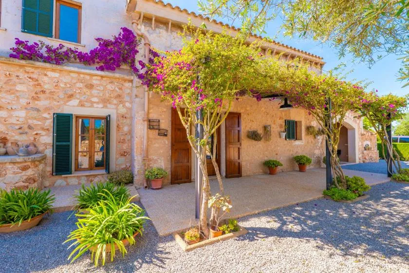 Exterior de una casa de piedra con entrada sombreada y enredaderas floridas.