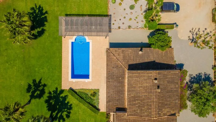 Una vista aérea muestra una piscina junto a un edificio de techo de tejas y jardines.