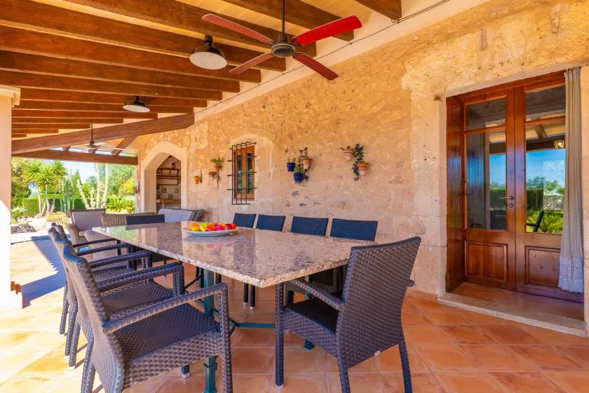 Un comedor exterior cubierto tiene una mesa larga y asientos tejidos.