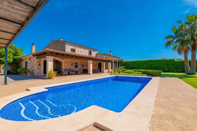 Una piscina al aire libre junto a un patio cubierto y un jardín cuidado.
