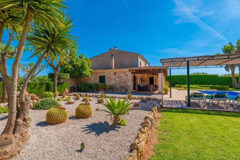 Una casa de piedra da a un jardín de grava y una zona de estar al aire libre con sombra.