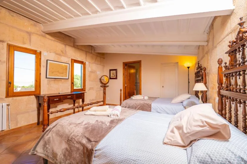 Un dormitorio con dos camas, muebles de madera y ventanas en las paredes de piedra.