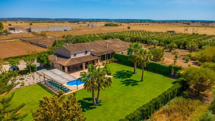Una casa rural da a un césped verde, una piscina y campos circundantes.