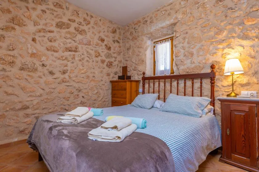 Un dormitorio con cama de madera, ropa de cama a rayas y paredes de piedra vista.