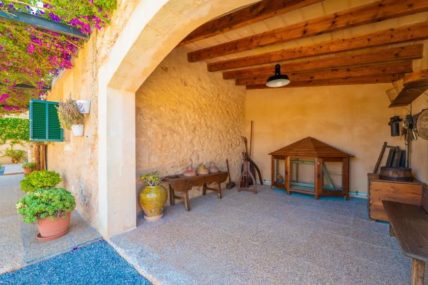 Un patio cubierto con techo de vigas de madera, asientos y plantas en macetas.