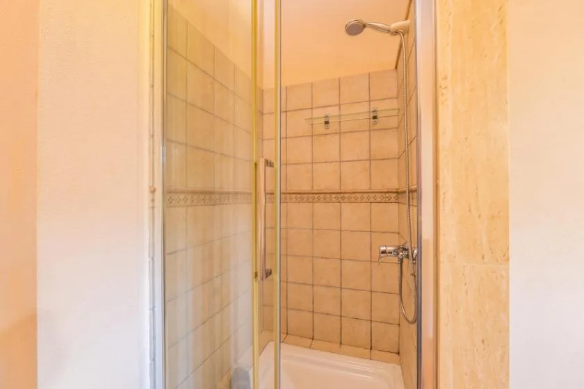 Una zona de ducha con azulejos, mampara de vidrio y cabezal de ducha en la pared.