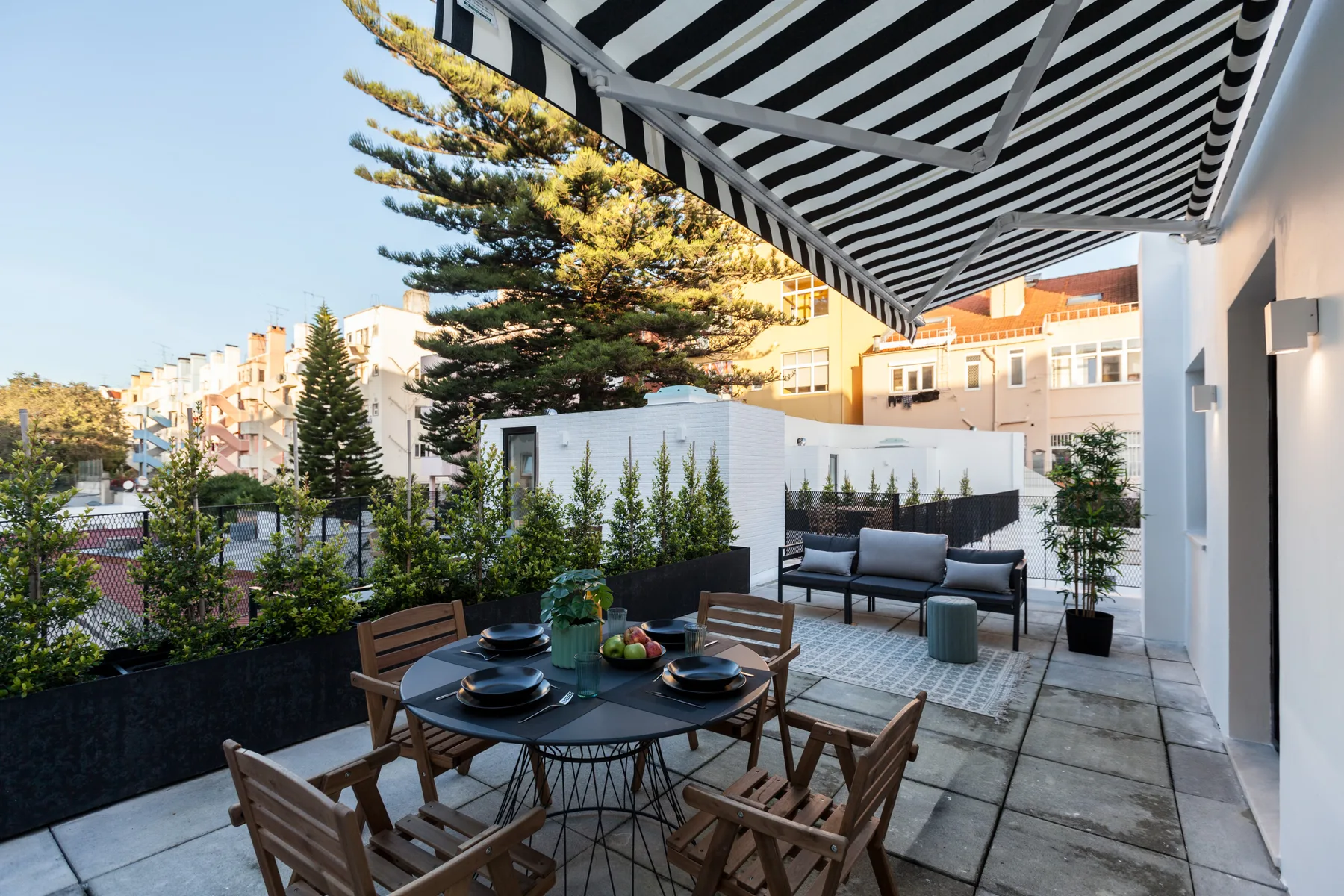 A furnished outdoor terrace with dining seating, lounge seating, and a striped awning.