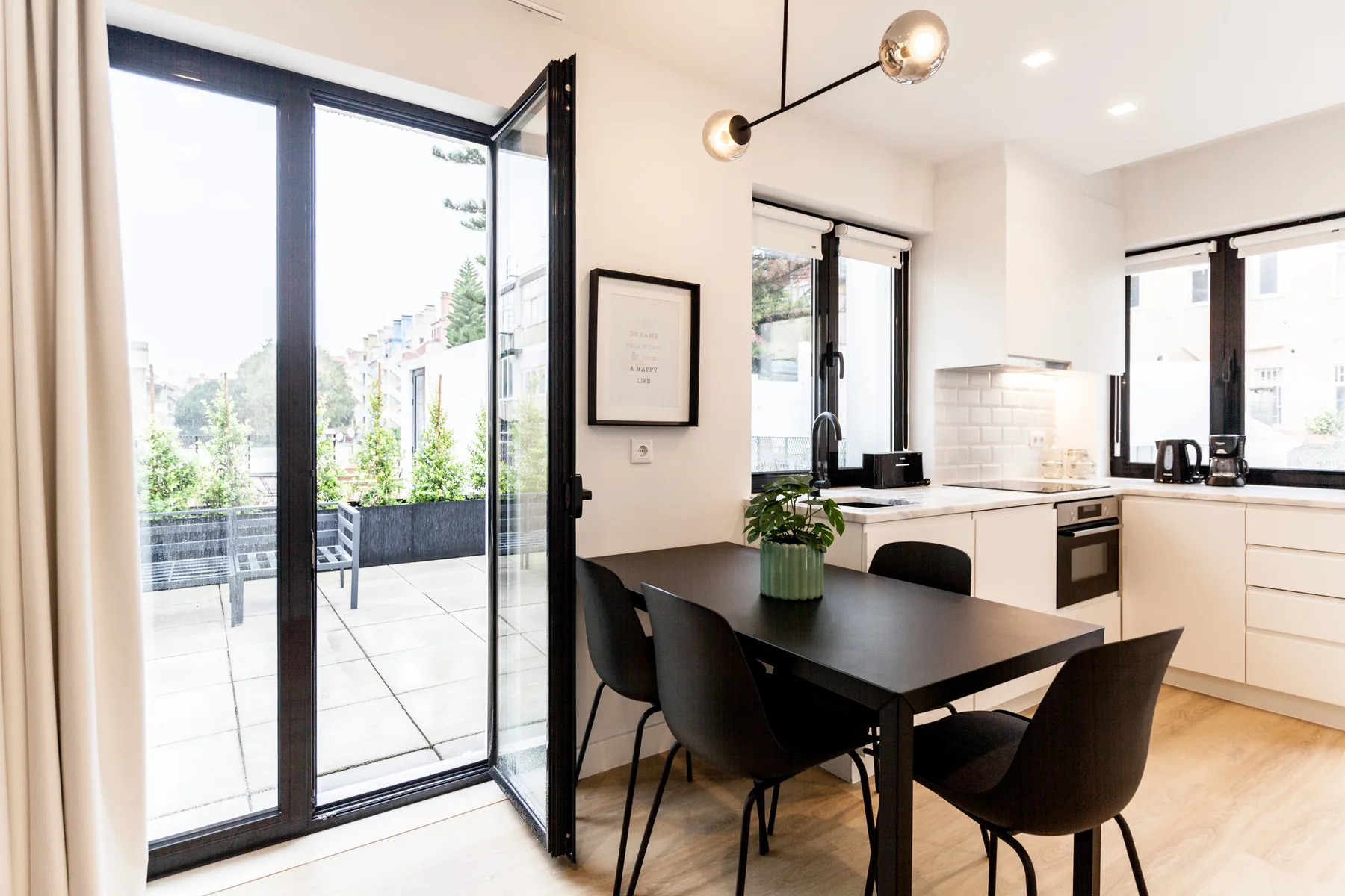 A bright dining area with a black table and an open glass door to a balcony.