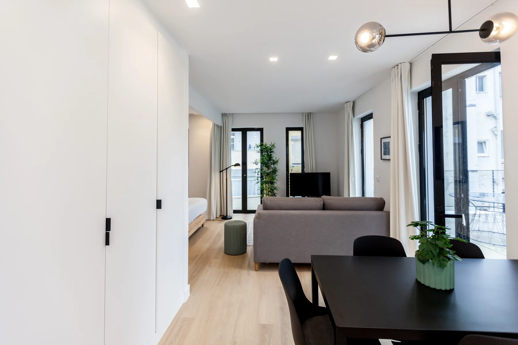 Bright studio living and dining area with a sofa, table, and large windows.