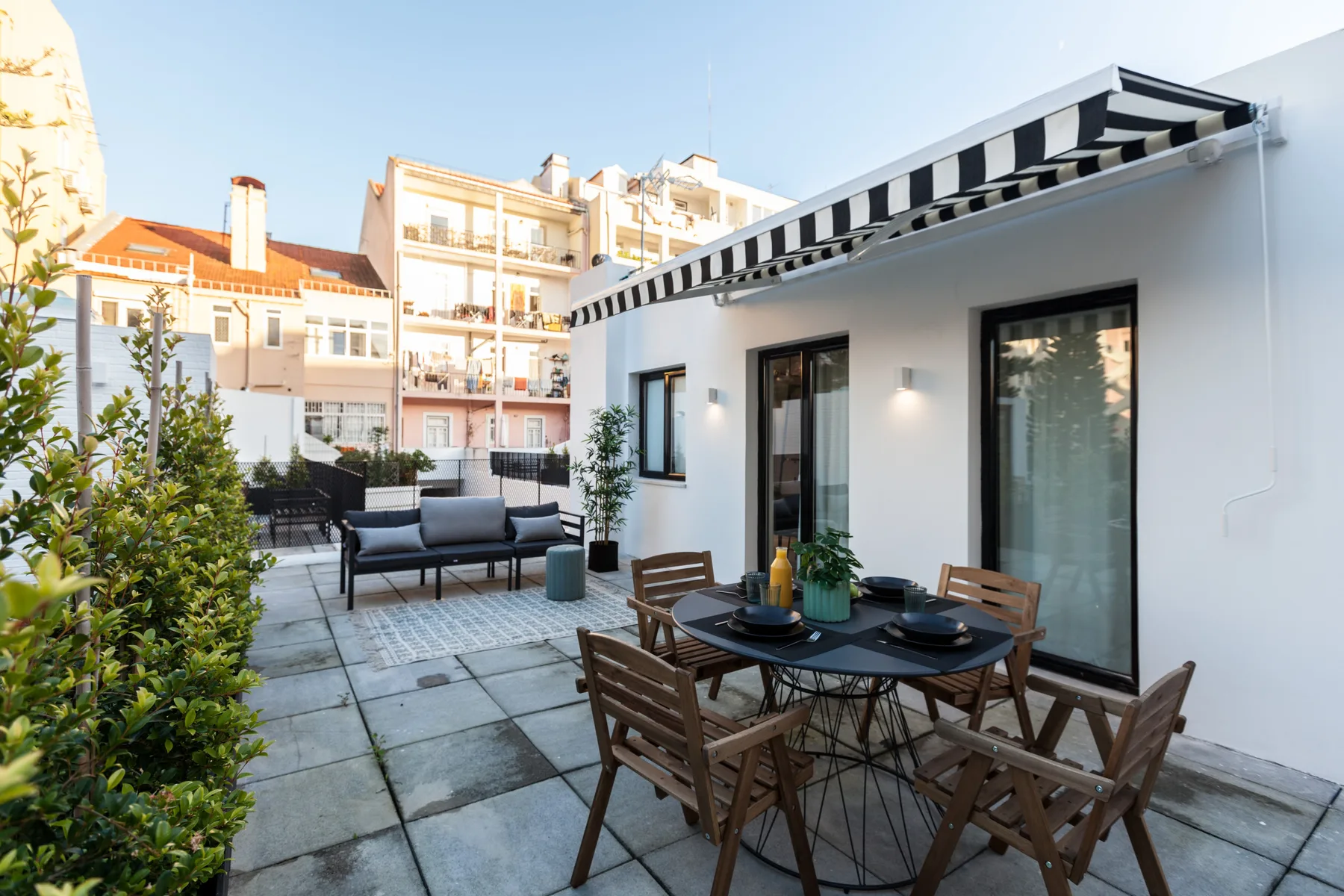 A furnished outdoor patio with a dining table, seating, and a striped awning.