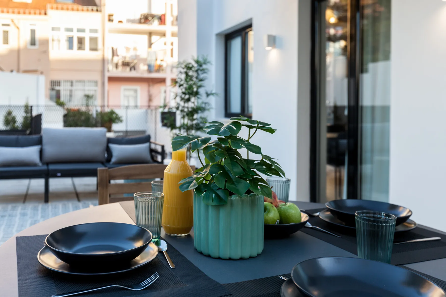 A dining table with place settings and a potted plant overlooks a furnished patio.