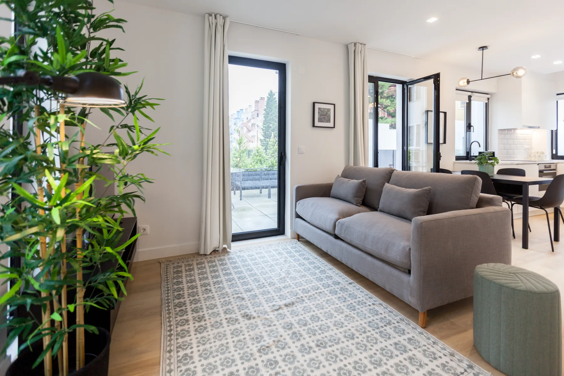 A bright living room with gray seating and a dining area beside the windows.
