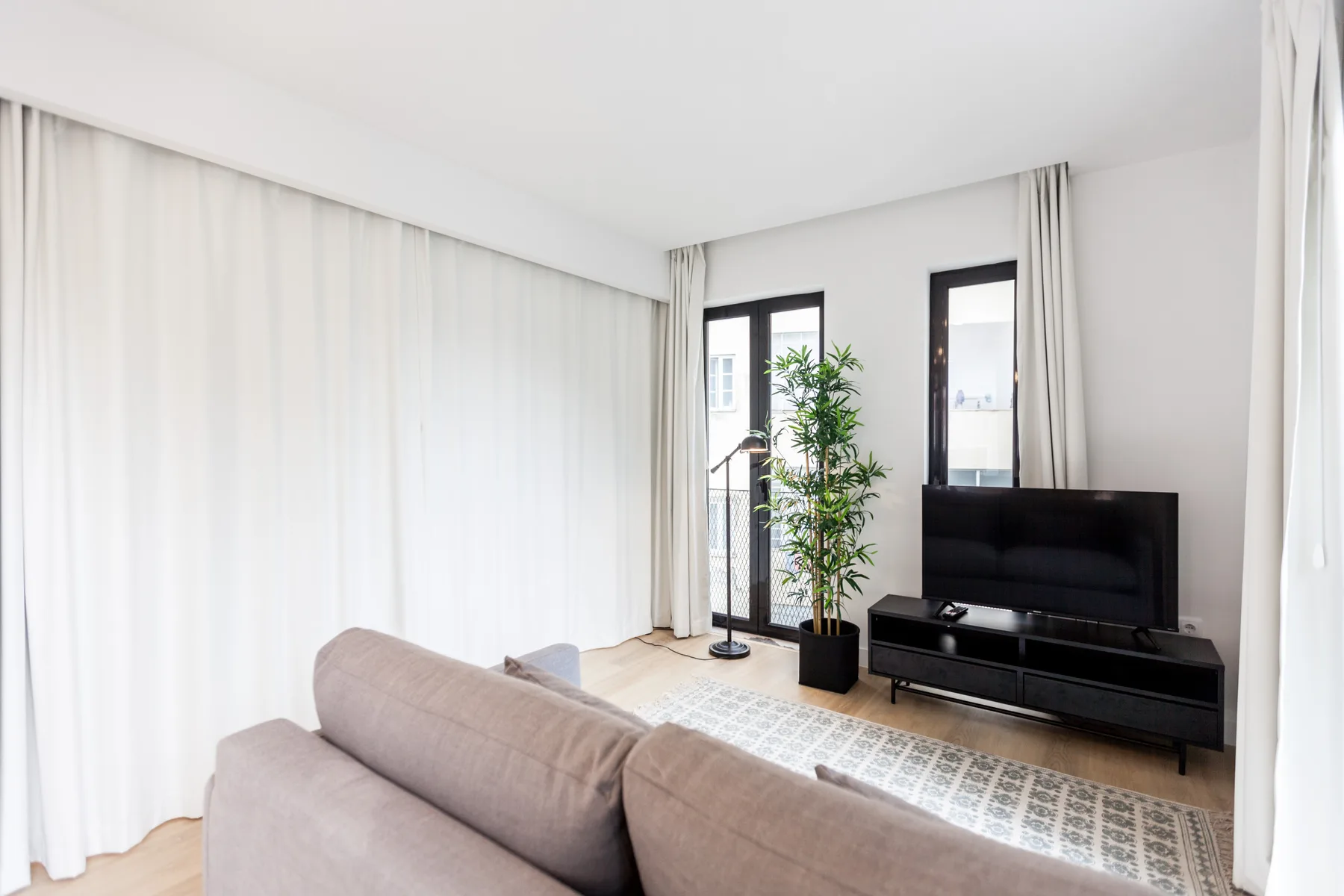 A bright living room with seating, a television, and tall curtains.