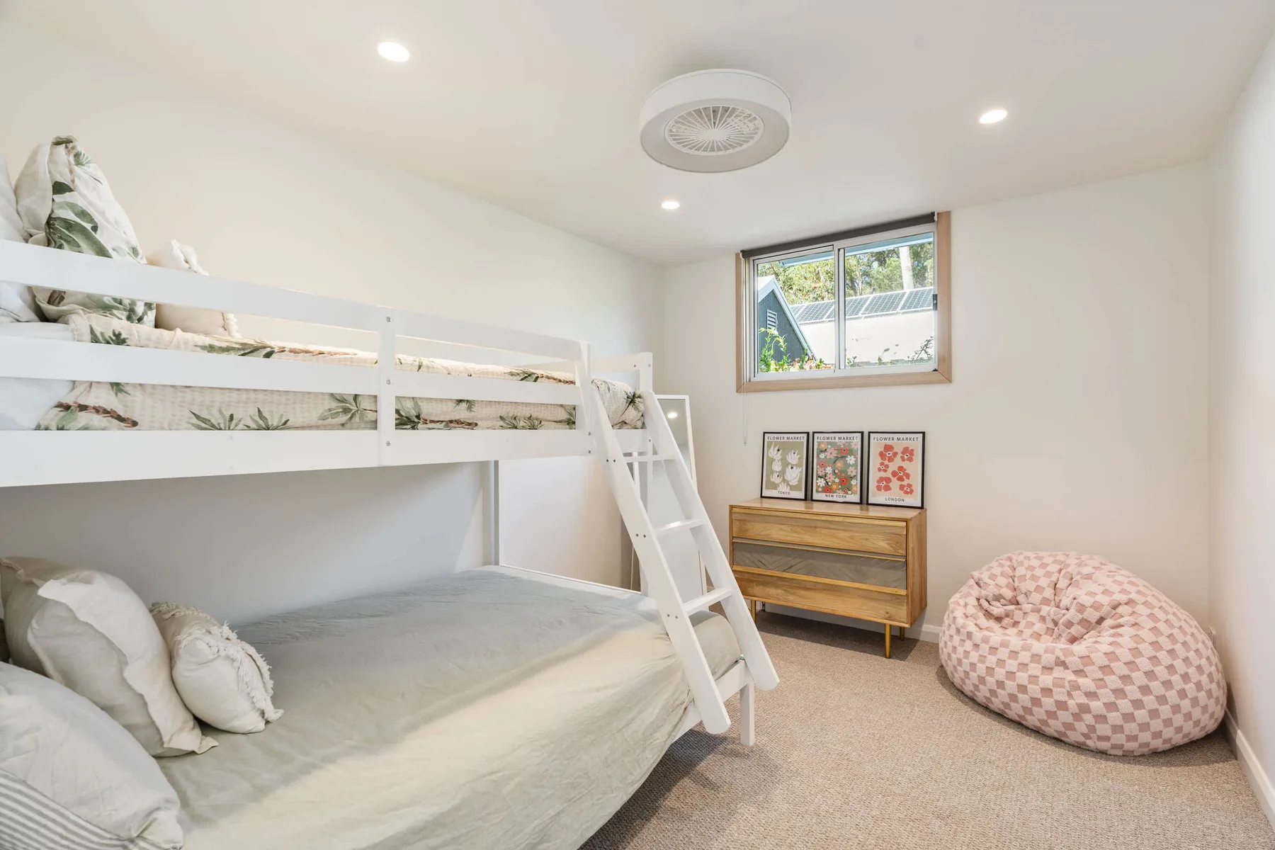 A bright bedroom with bunk beds, a window, and a beanbag chair.