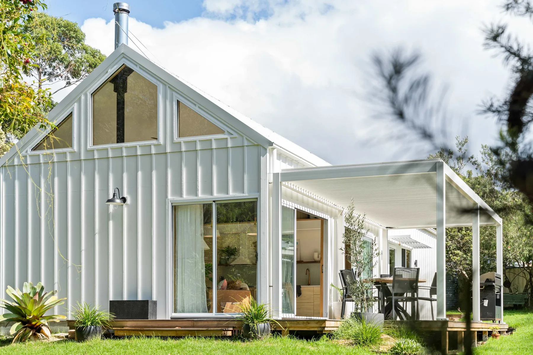 A light-colored barn-style house with a covered outdoor seating area.