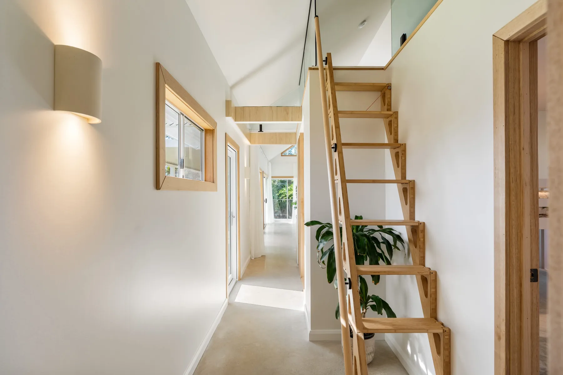 A bright hallway with a wooden staircase and a window at the far end.