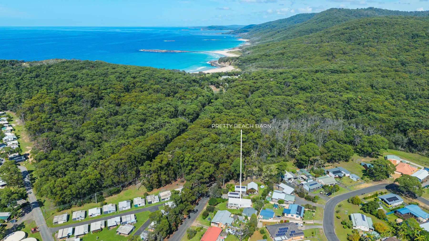 Aerial coastal scene with forested hills, a settlement, and the ocean.