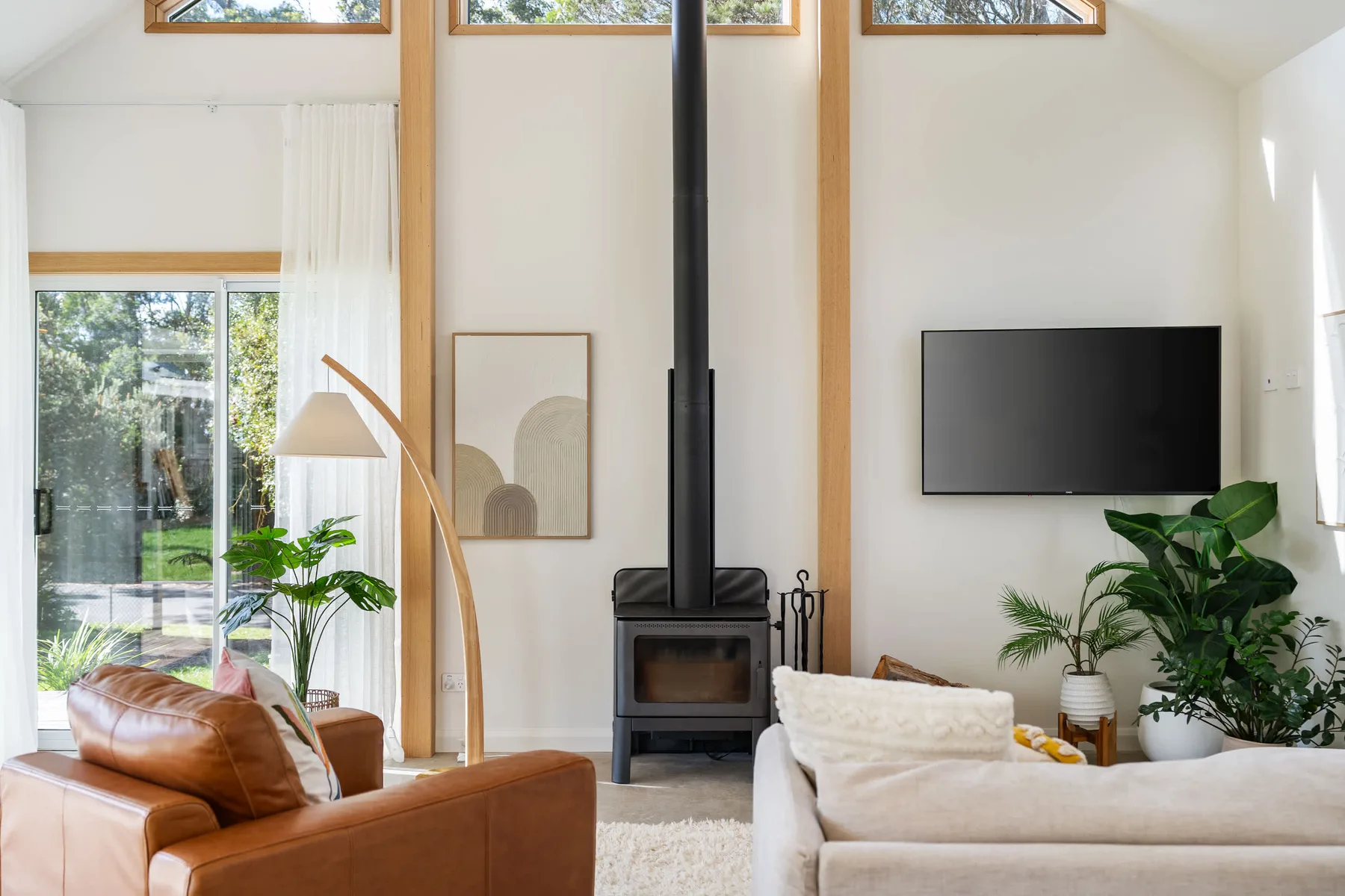 A bright living room with seating, a freestanding stove, and a wall-mounted television.