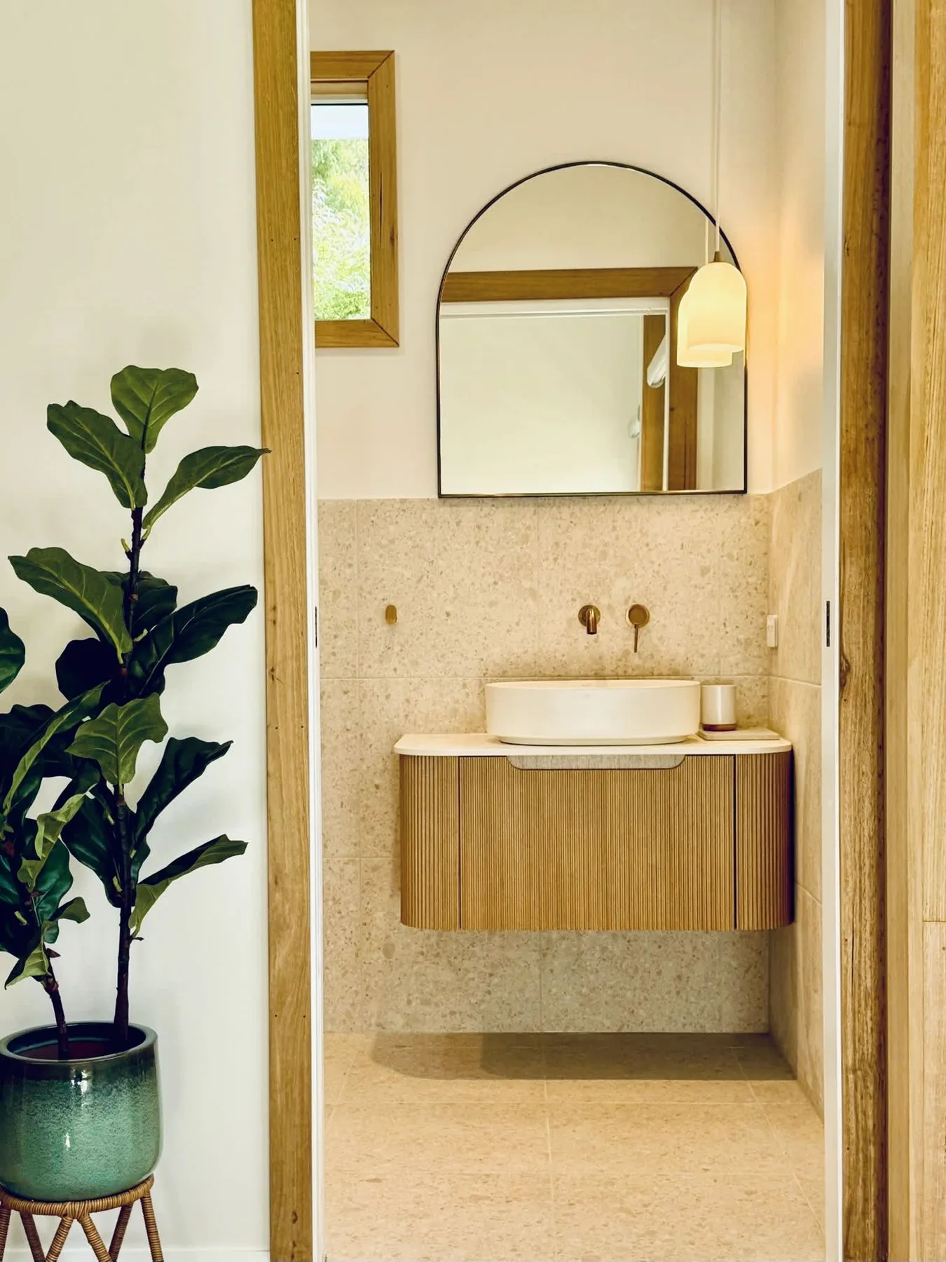A bathroom vanity with a vessel sink, wall-mounted faucet, and arched mirror.