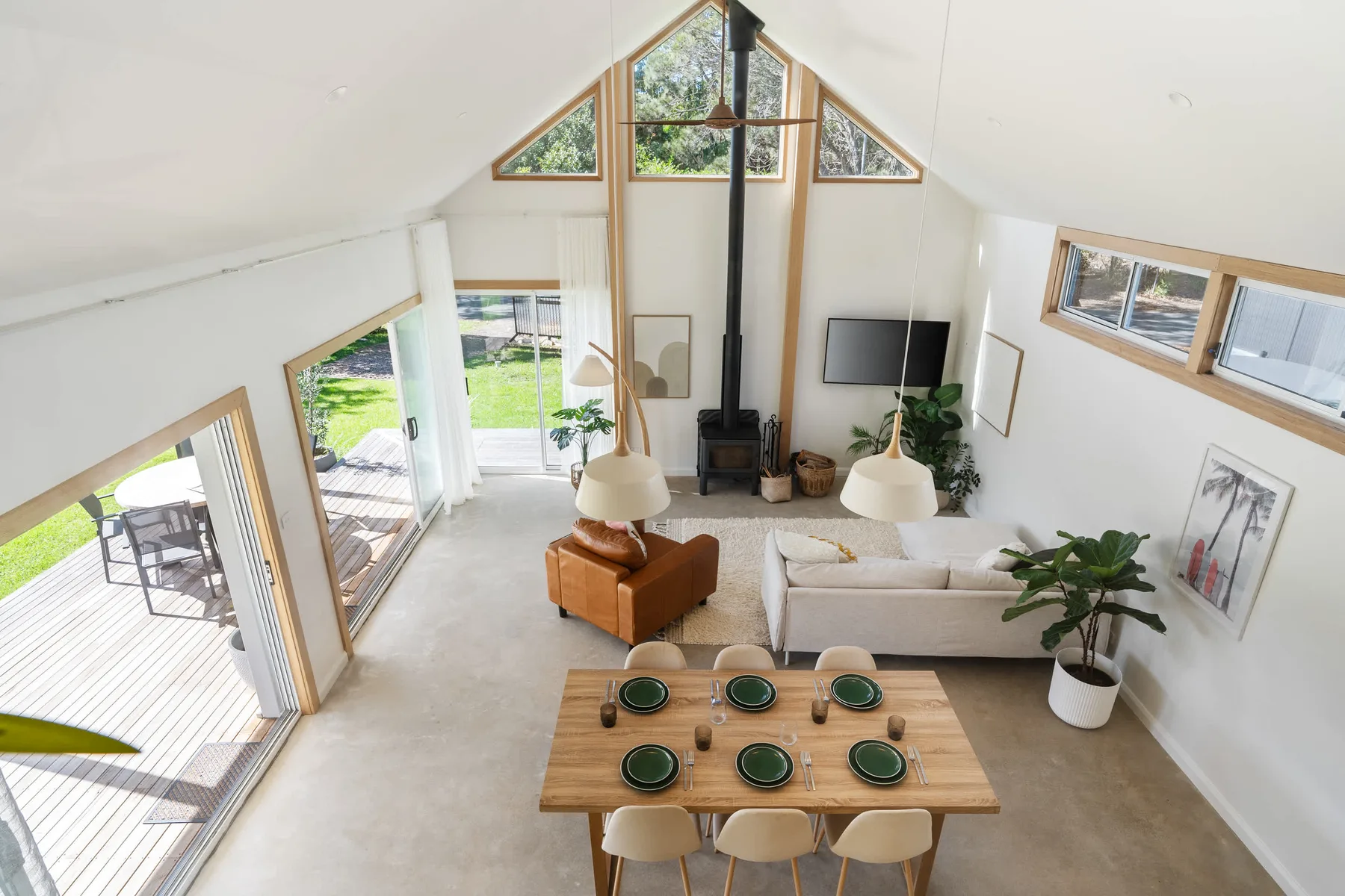 A bright open-plan living and dining area has a high sloped ceiling and large windows.