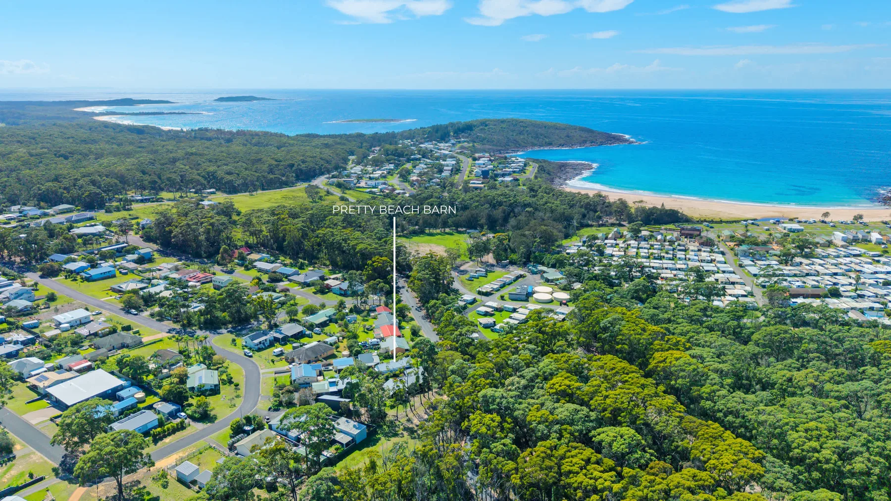 Aerial view of a coastal town, with homes, green woodland, and a sandy beach.