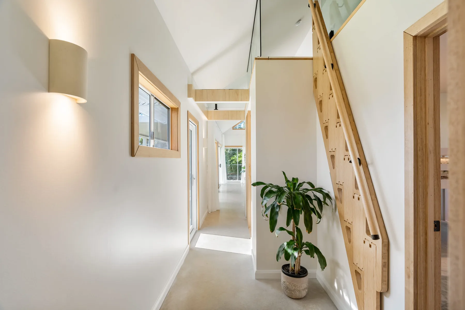 A bright hallway with a potted plant and a wooden staircase.