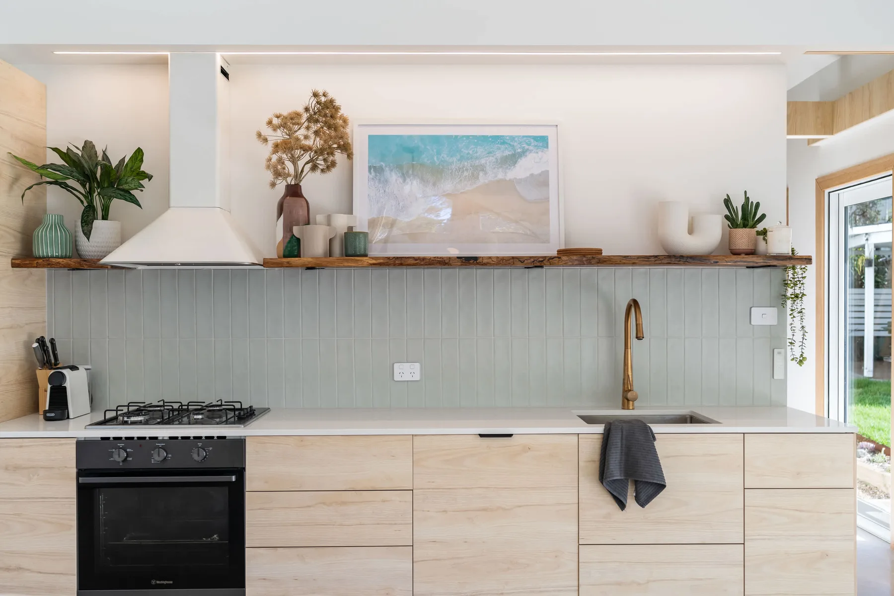 A bright kitchen with pale cabinetry, a cooktop, and a sink beneath open shelving.