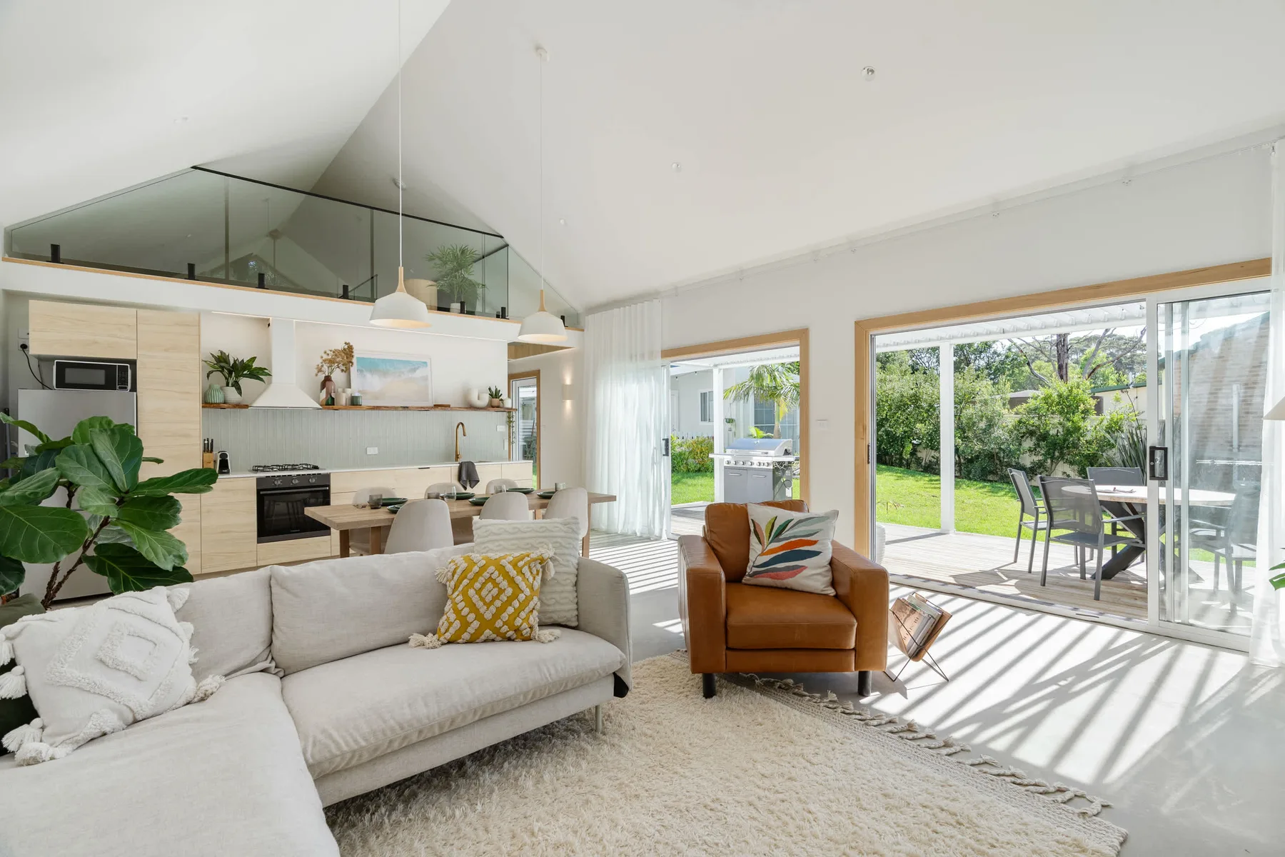 A bright living room opens onto a patio, with a kitchen behind the seating area.