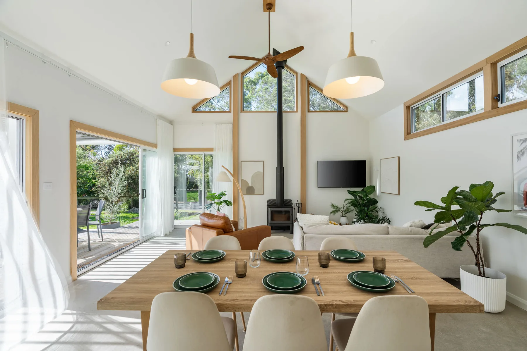 A bright open-plan living and dining area with a wooden table and garden views.