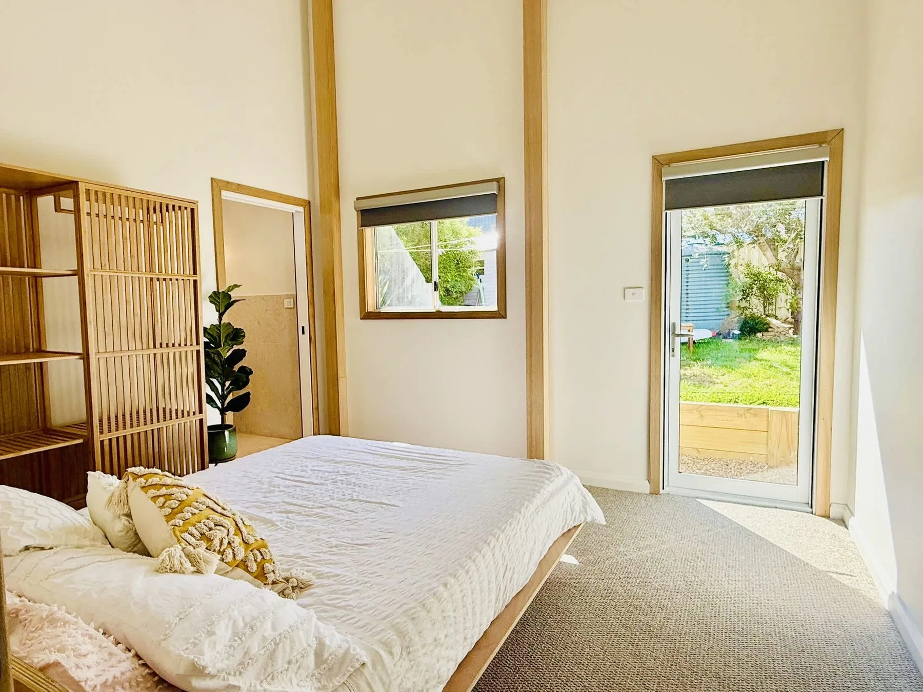 A bright bedroom with a bed and windows overlooking a garden.