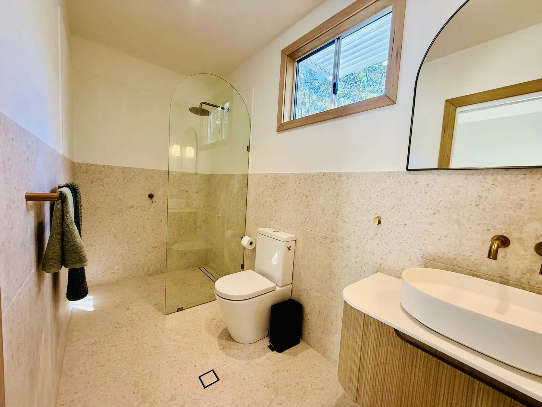 A bathroom with a shower, toilet, and sink beneath a high window.