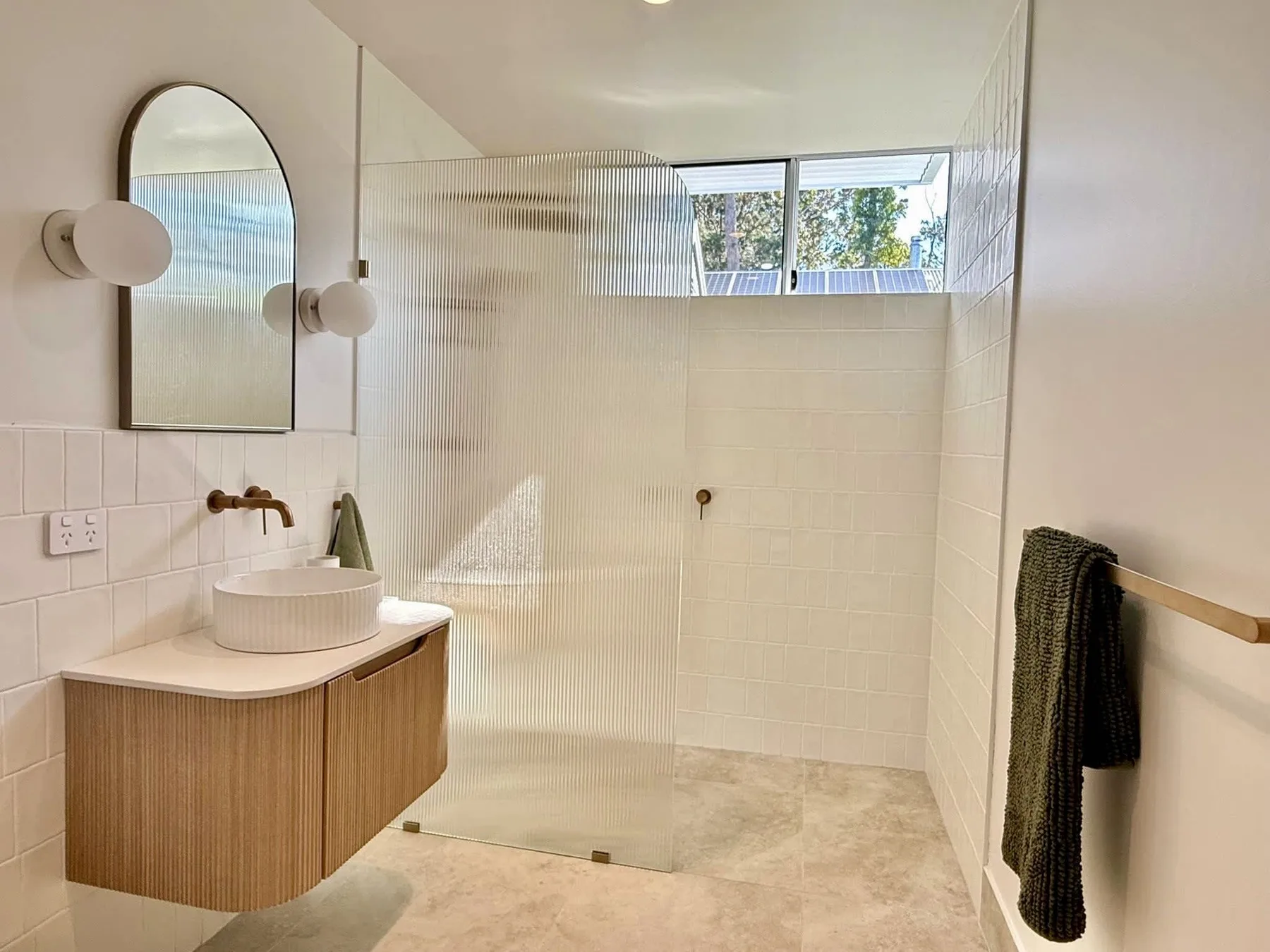 A bright bathroom has a wall-mounted vanity and a glass shower.