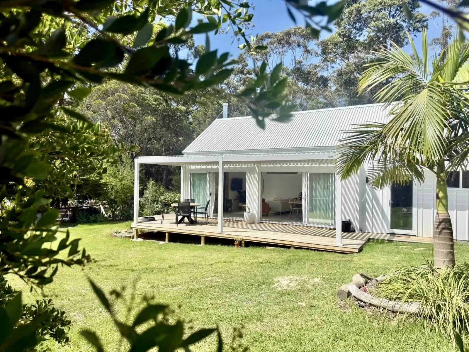 A white house with a covered deck stands beside a grassy lawn and trees.