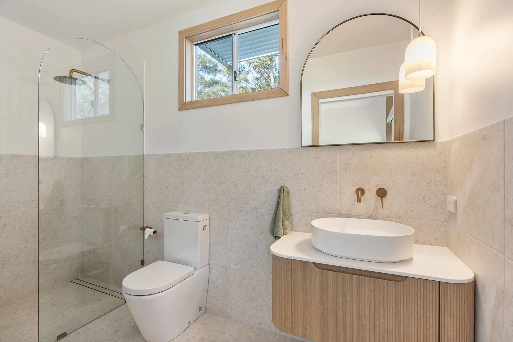 A bright bathroom with a glass shower, toilet, and sink vanity.