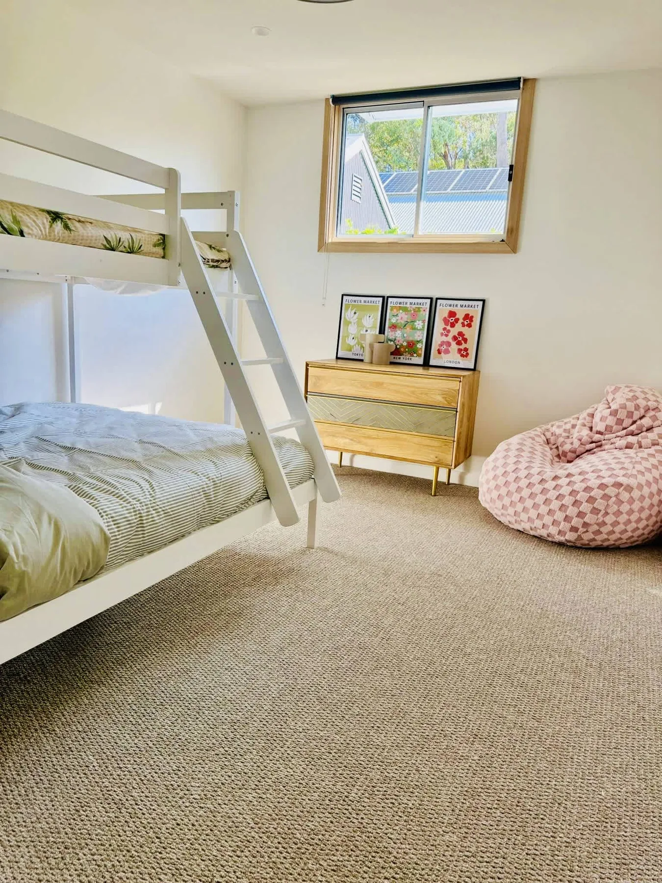 A bright bedroom with bunk beds, a dresser, and a patterned beanbag.