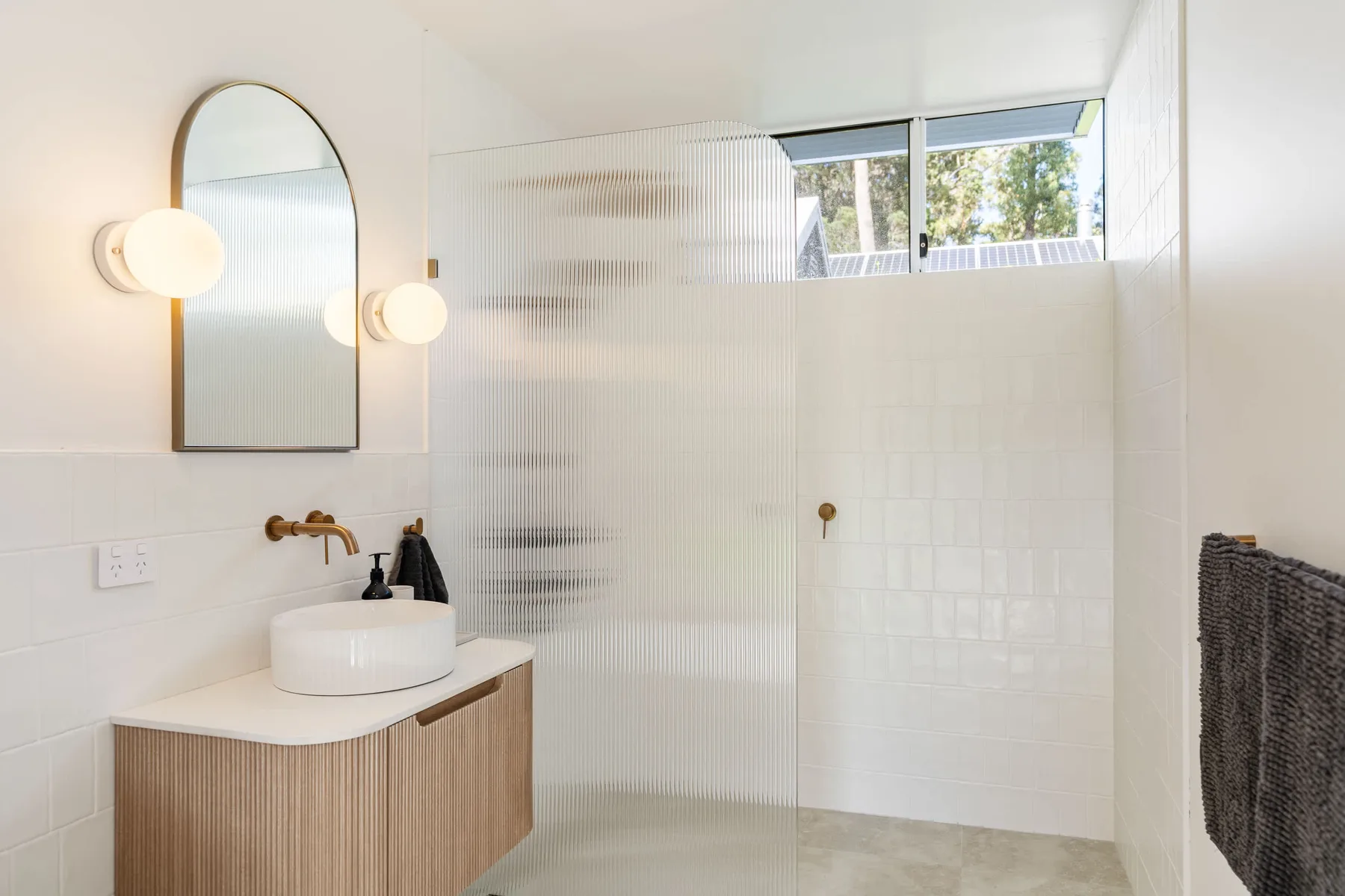A bright bathroom with a sink, mirror, and glass shower.