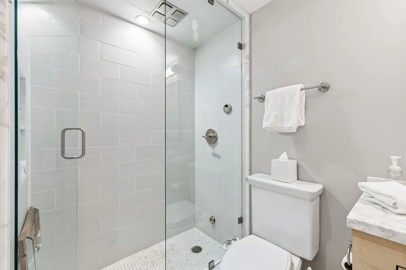 Un baño luminoso con ducha de vidrio y azulejos blancos.