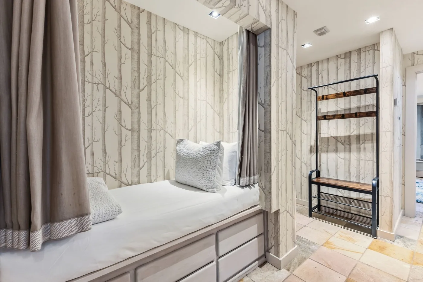 Un dormitorio con una cama empotrada bajo un papel pintado con motivos de árboles.