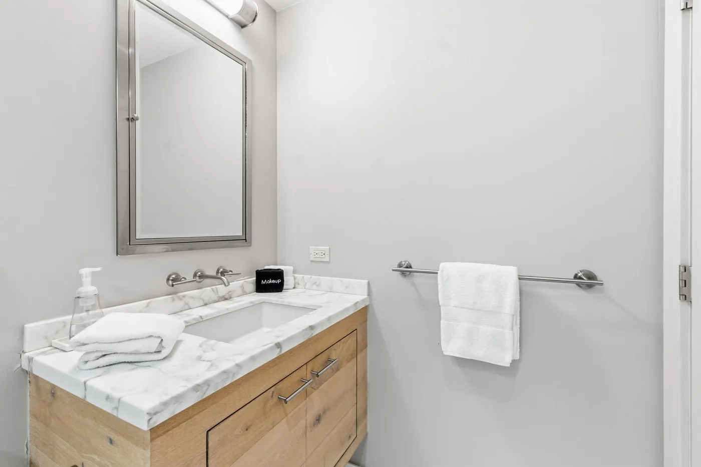 Un tocador de baño luminoso con un espejo y una toalla doblada sobre la encimera.