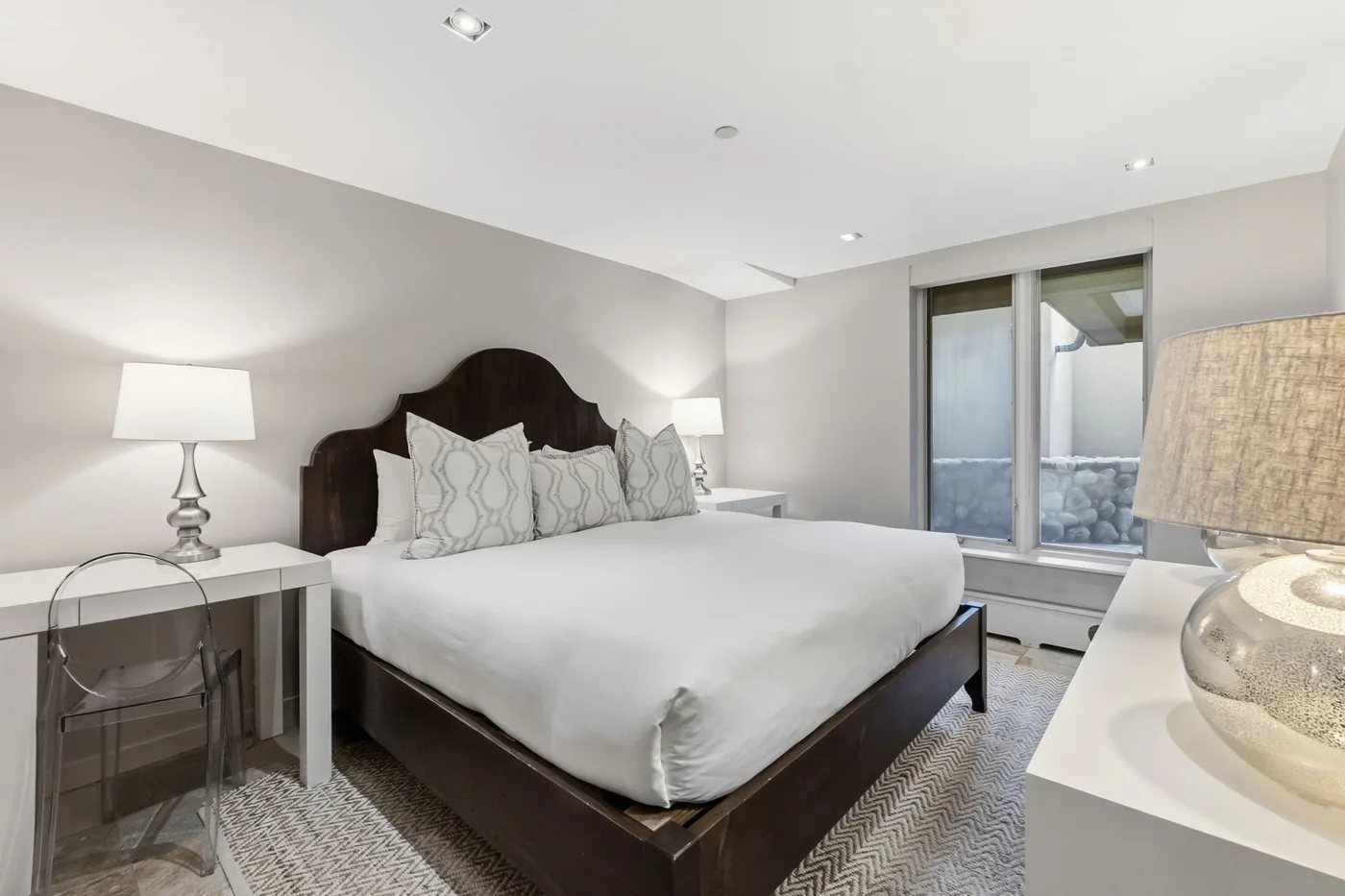 Dormitorio luminoso con una cama grande, almohadas estampadas y una ventana.