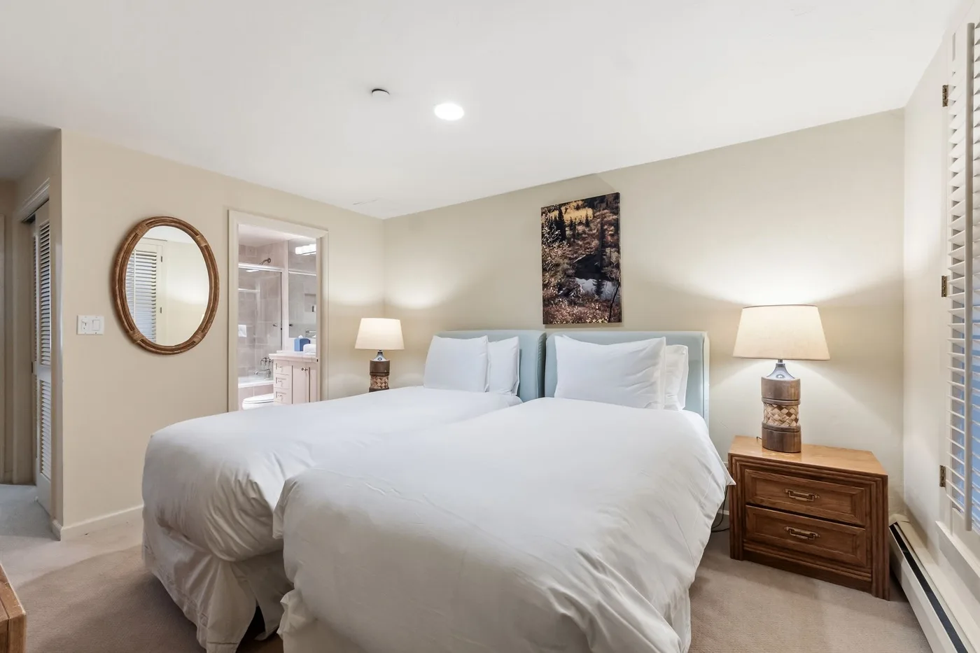 Un dormitorio con ropa de cama blanca, mesitas de noche y un cuadro sobre la cama.