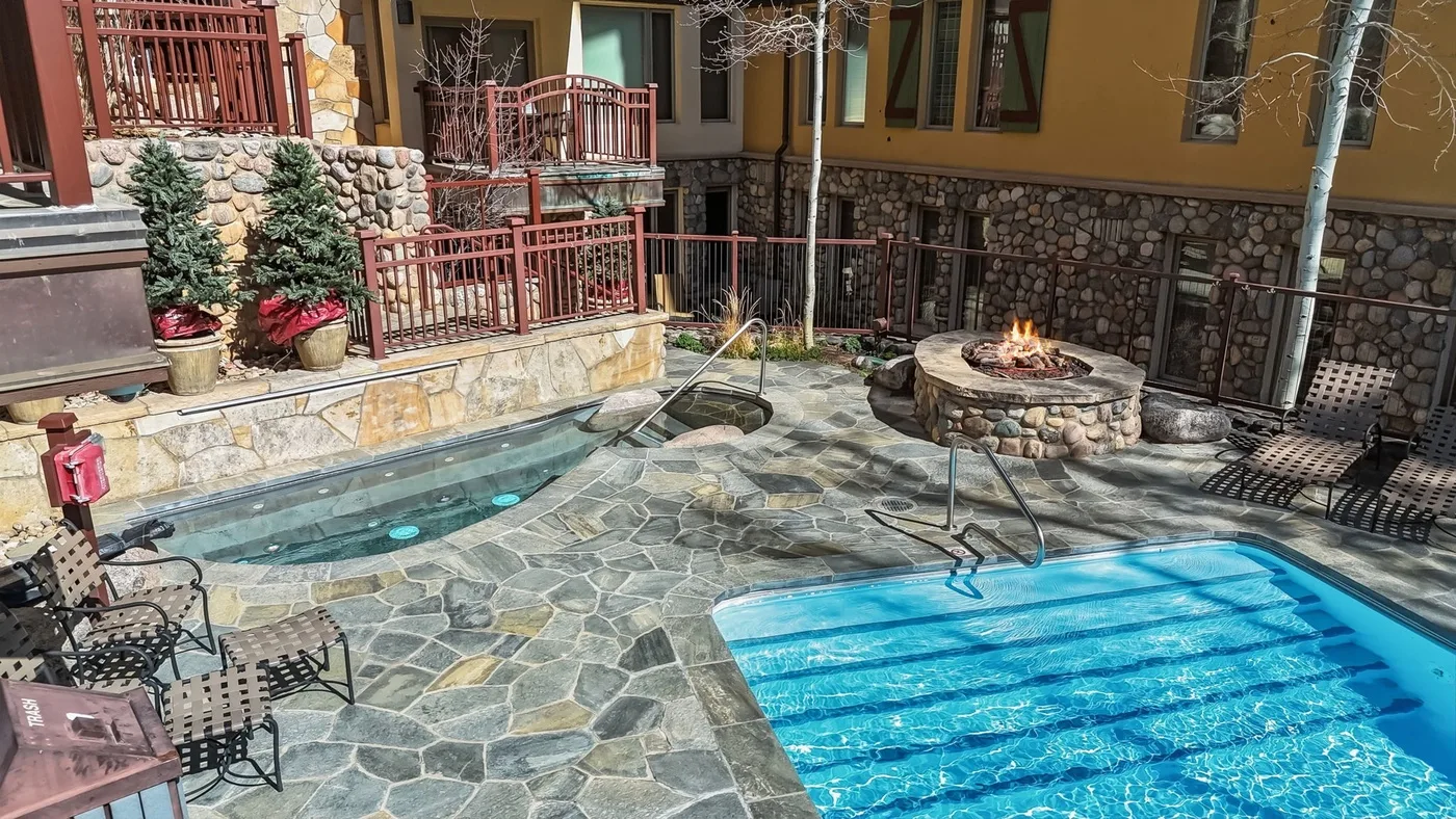 Una piscina exterior y una bañera de hidromasaje están junto a un patio de piedra.