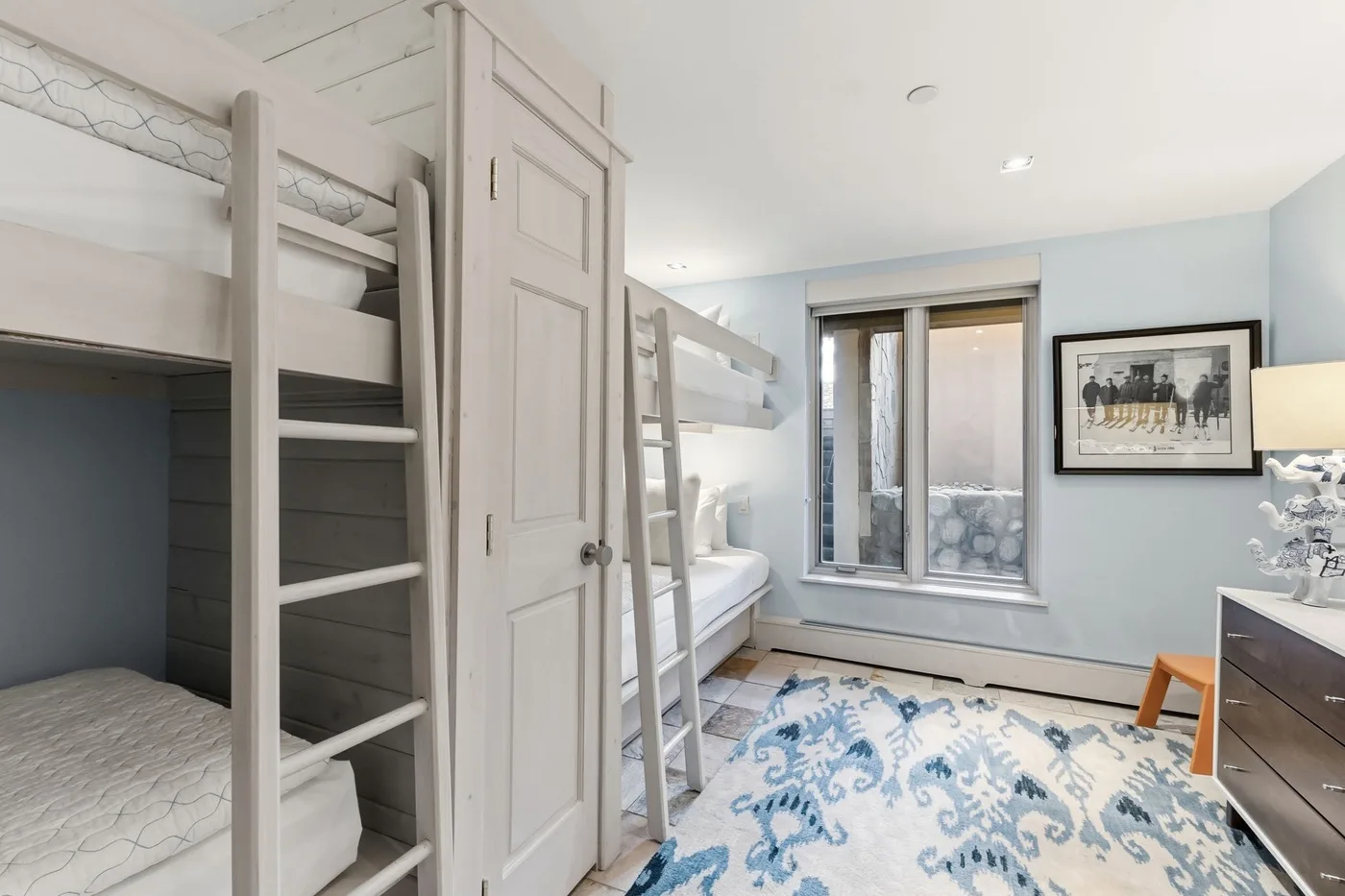 Un dormitorio luminoso con literas, una ventana y una alfombra estampada.