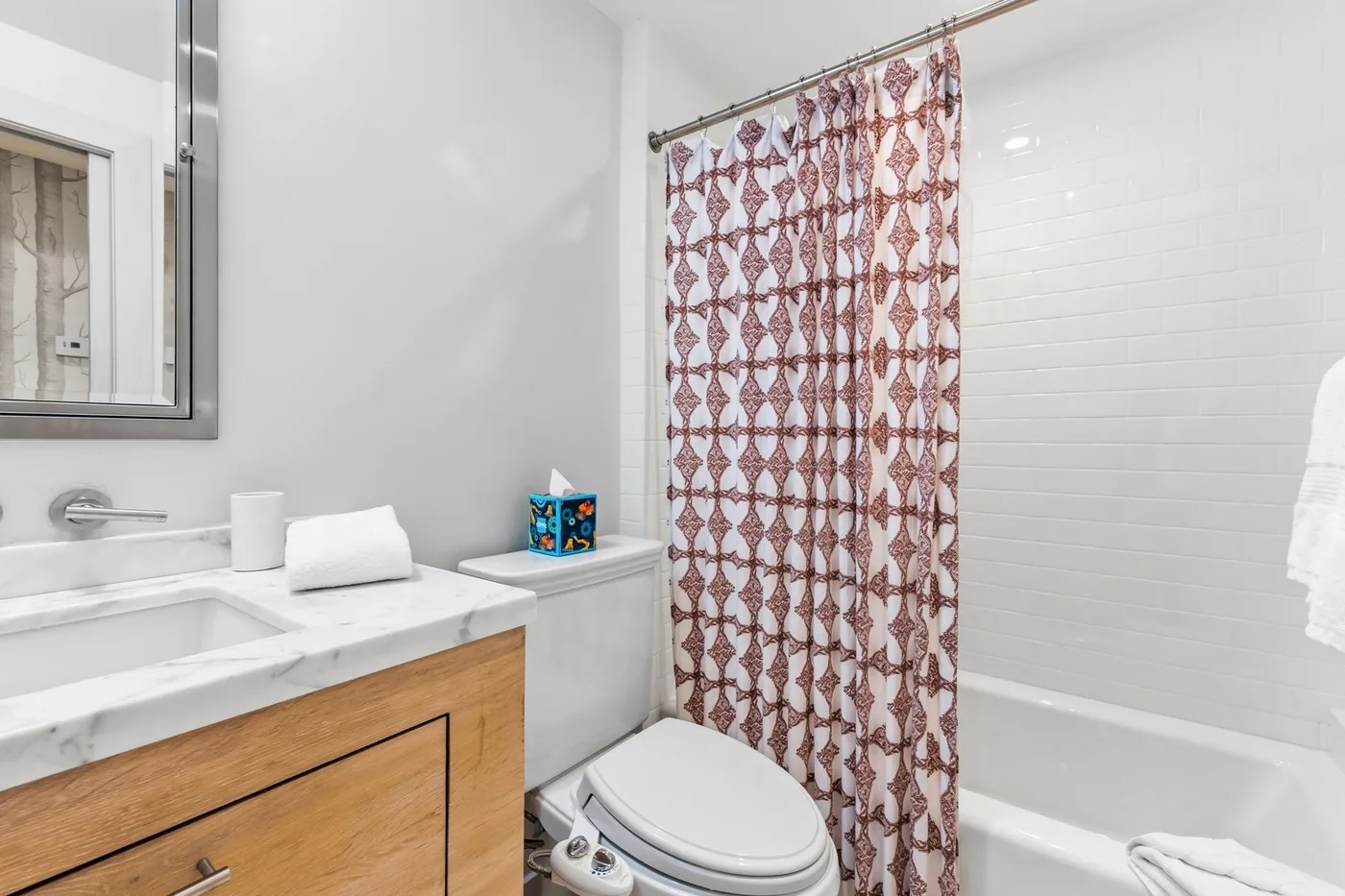Un baño con lavabo, inodoro y bañera detrás de una cortina estampada.