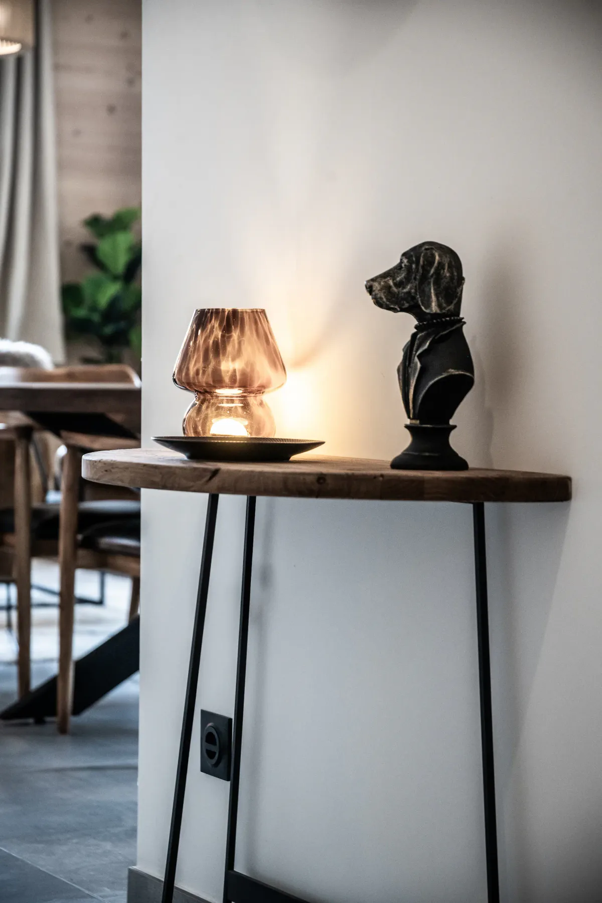 A small wooden table with a lit lamp and a dog-shaped sculpture in a cozy, modern living room setting.