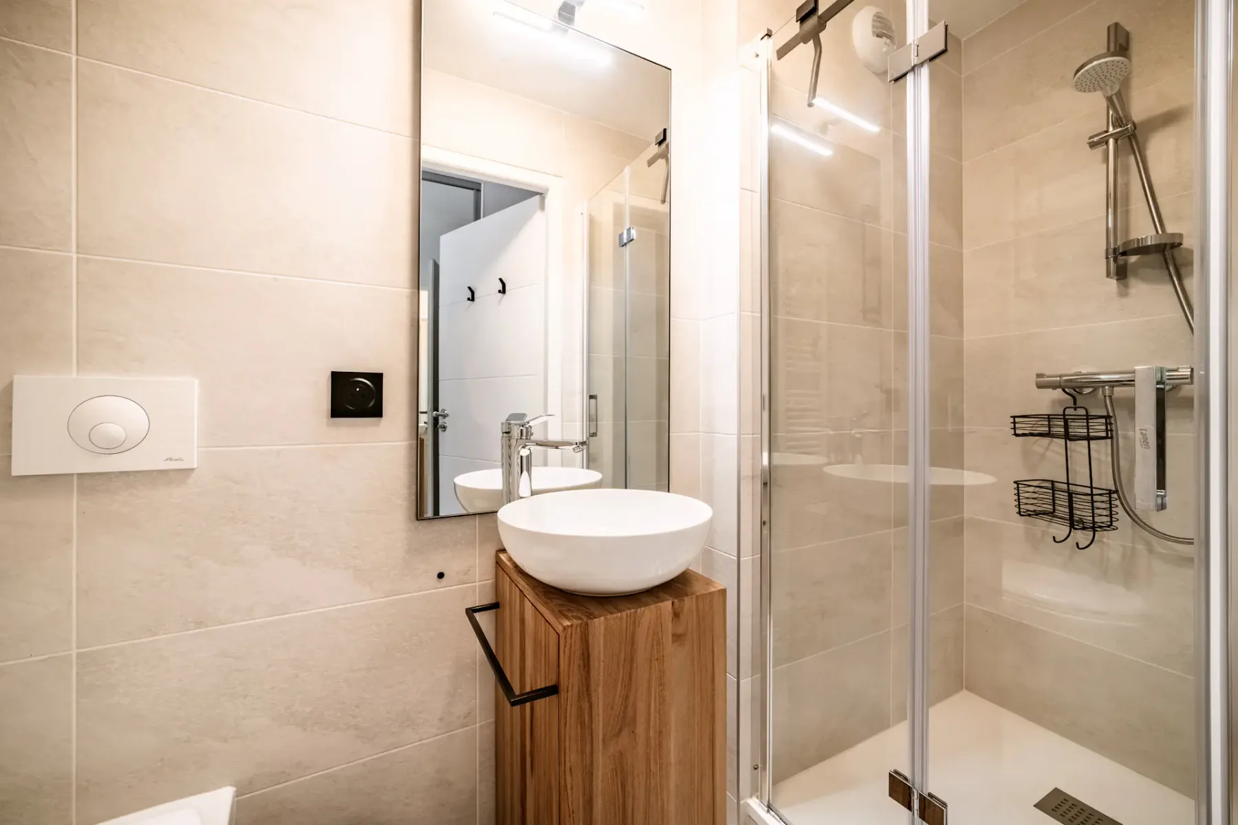 Modern bathroom with a glass shower, white sink on a wooden vanity, wall-mounted toilet, and beige tiles.