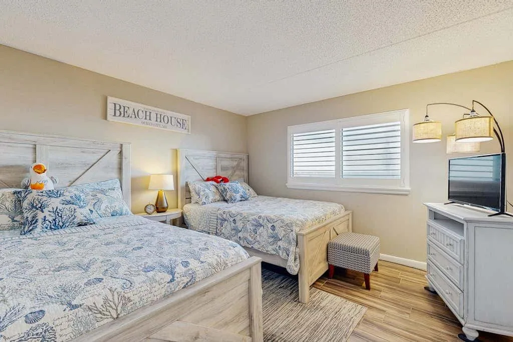 A bedroom with two beds, a window, and a dresser.